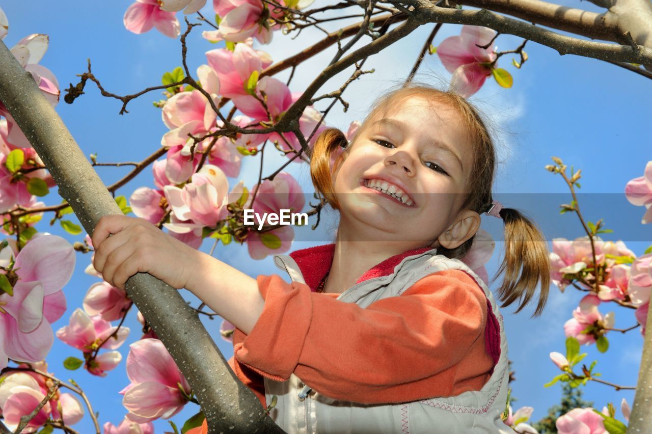 Low angle portrait of smiling girl amidst flowers on tree