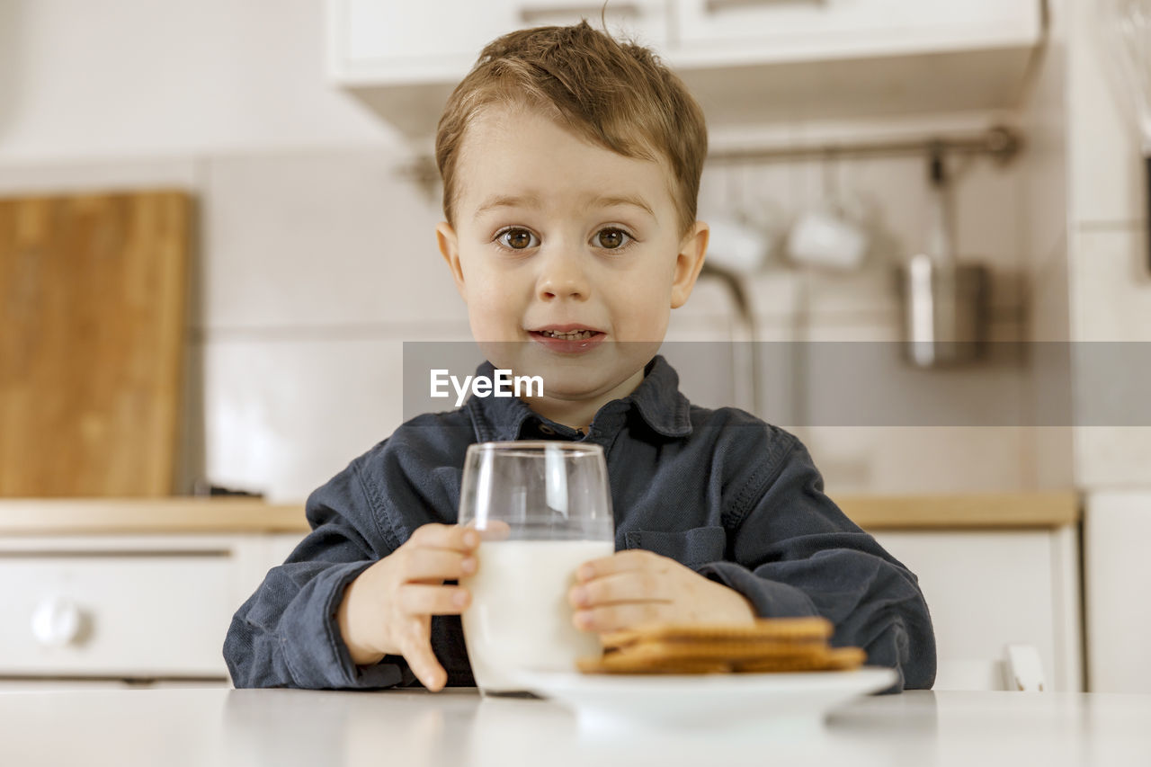 Little boy sitting in the kitchen and drinking milk. fresh milk in glass, dairy healthy drink. 