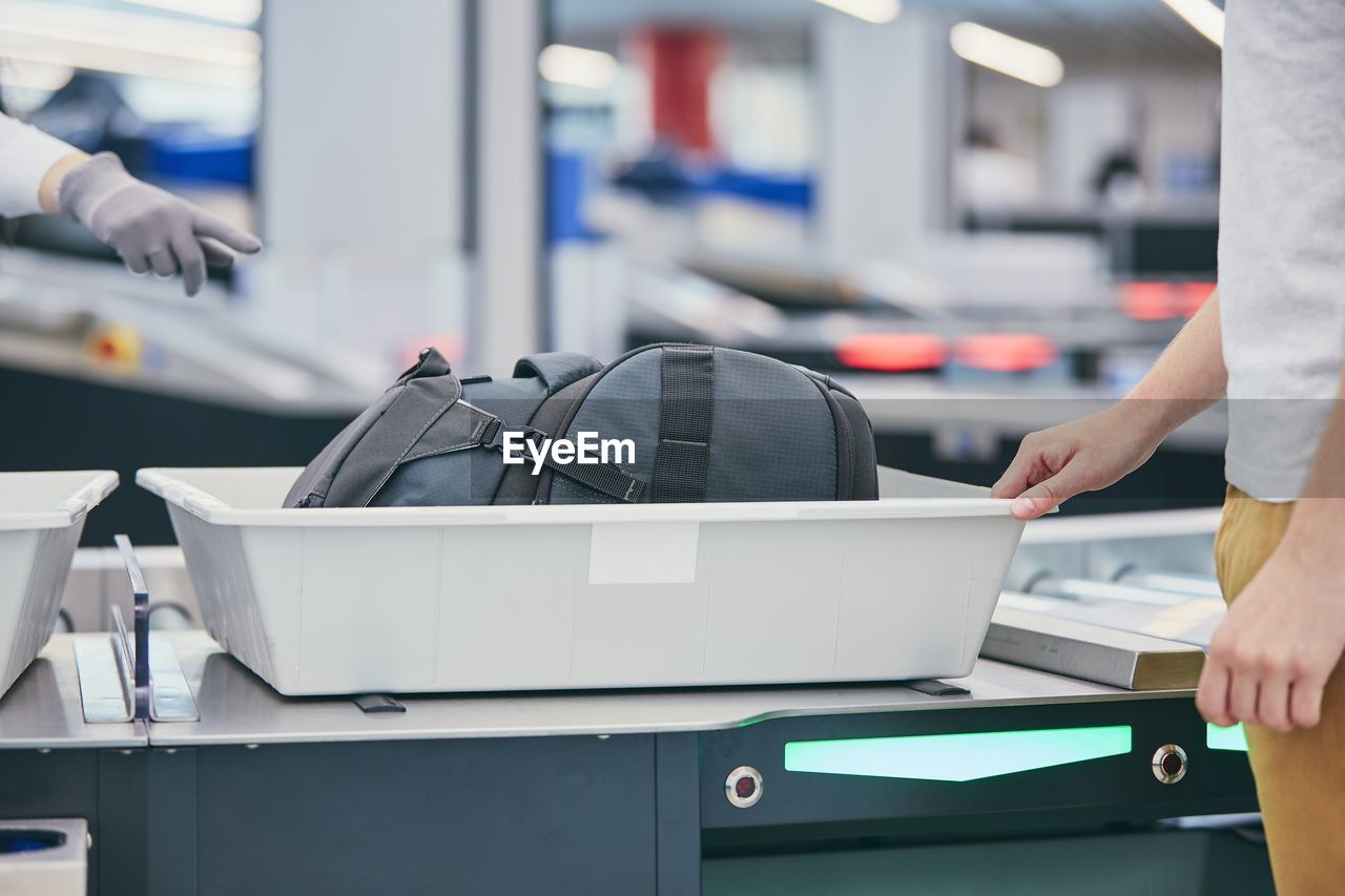 Midsection of man picking suitcase from conveyor belt