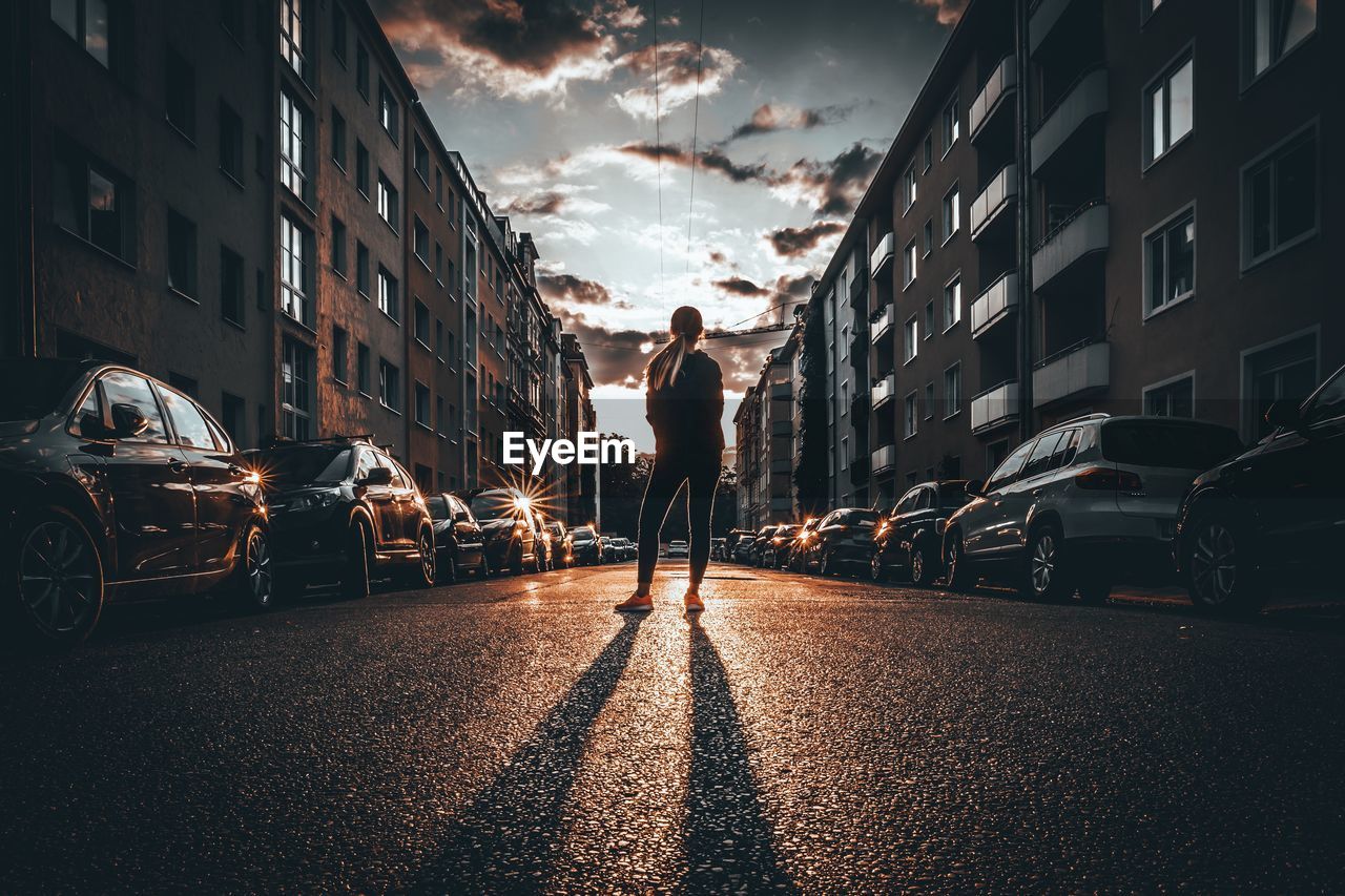 Rear view of woman standing on road in city against sky