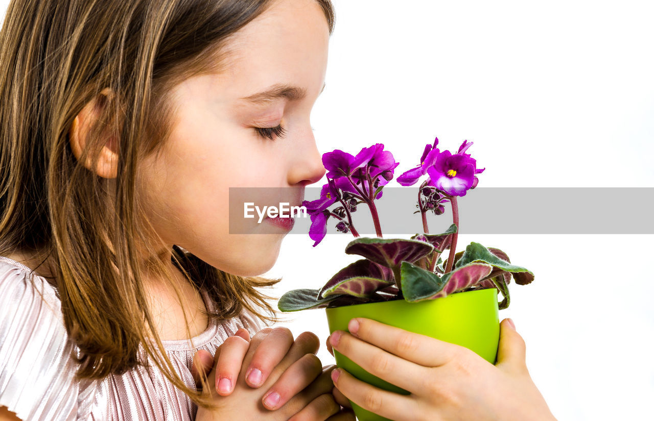 Side view of girl smelling flower held by sister against white background