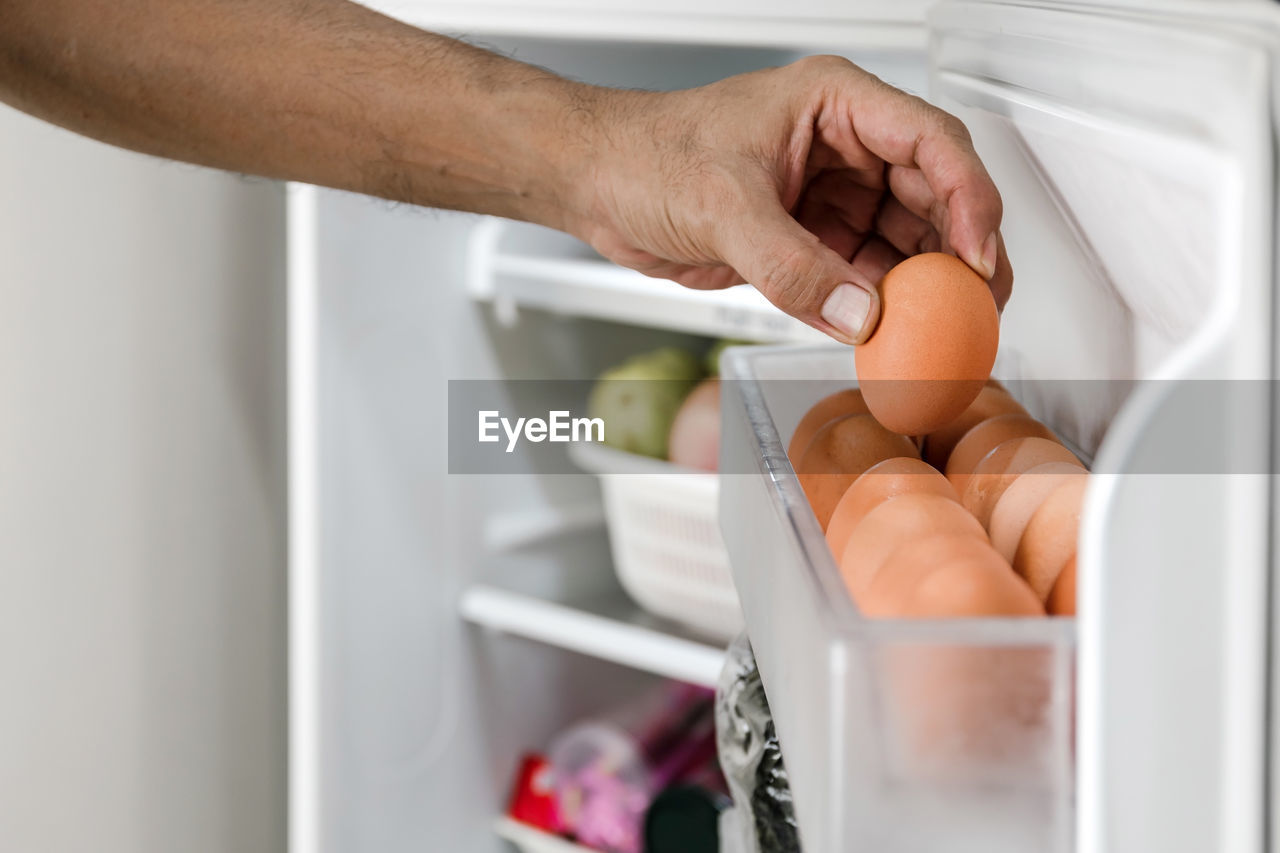 Close up human hands put chicken eggs in the egg-laying compartment in the refrigerator.