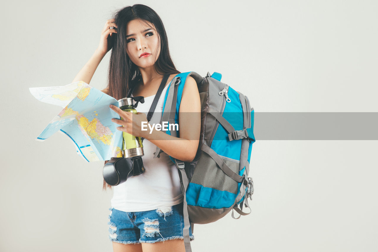 Young woman holding map while standing against white background