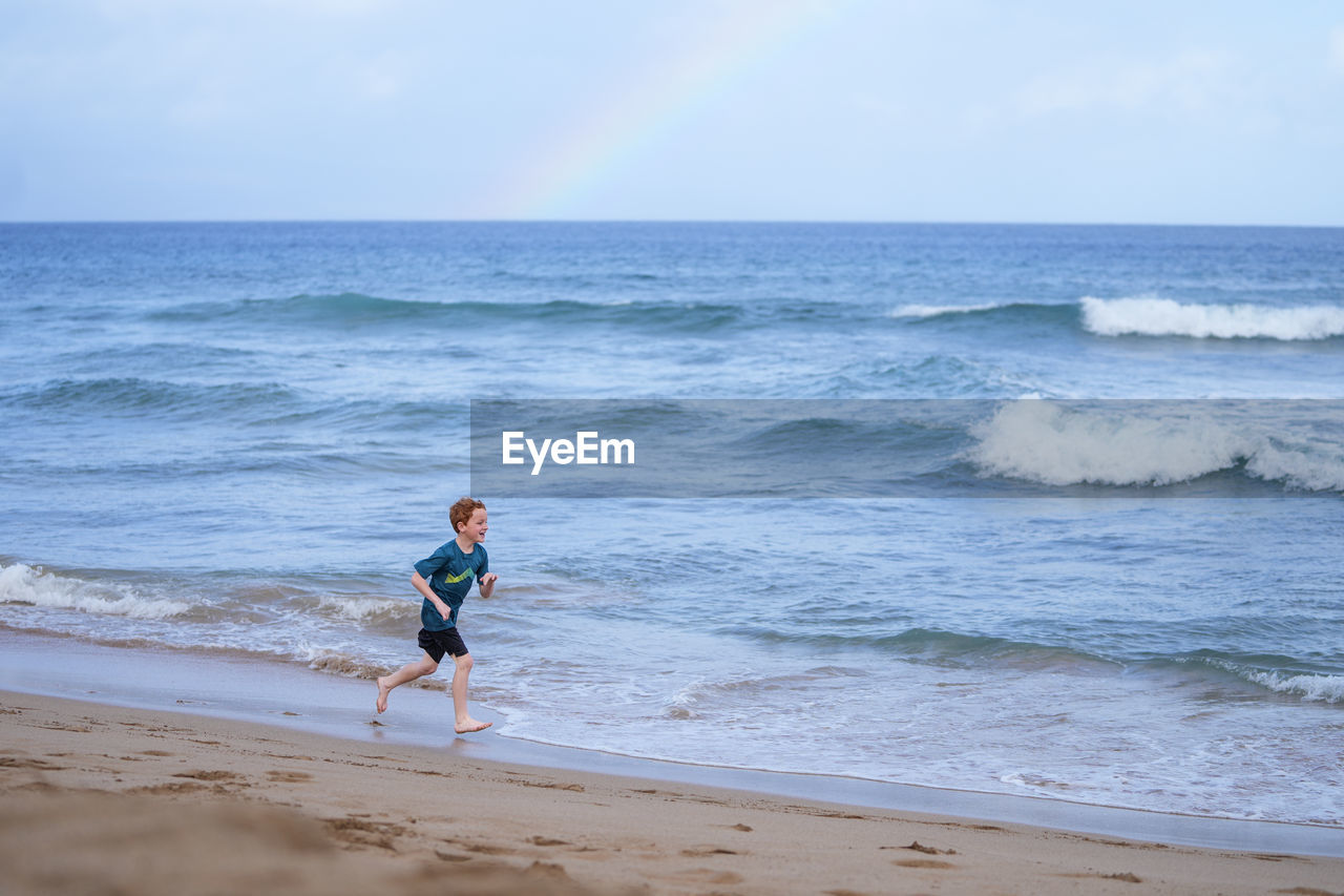 Young boy playing in the waves with a rainbow over the ocean on ka'anapali beach in hawaii. 