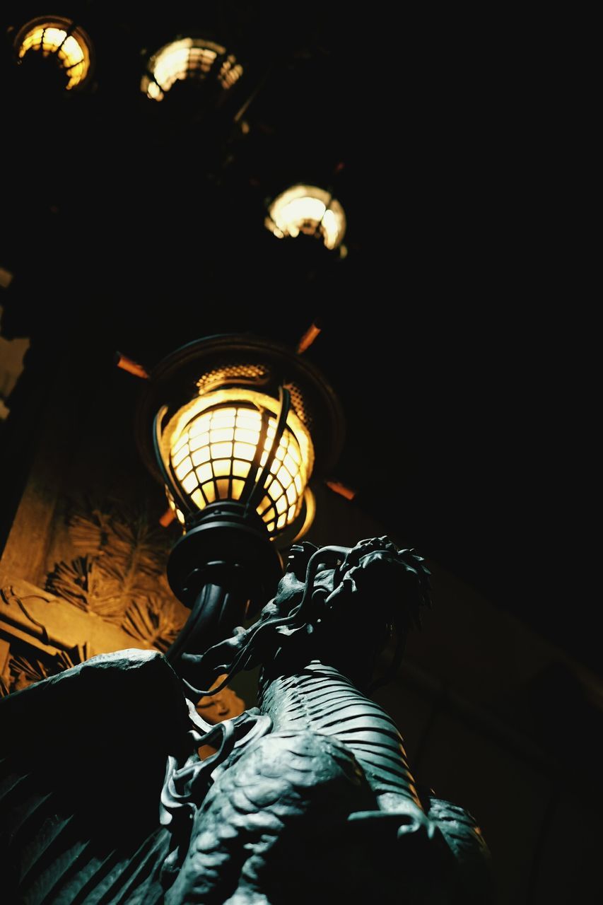 Low angle view of statue and illuminated lamp post at night