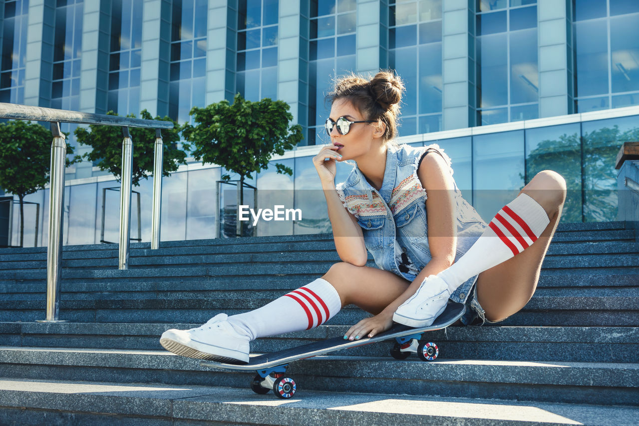 Full length of woman with skateboard sitting on steps outdoors