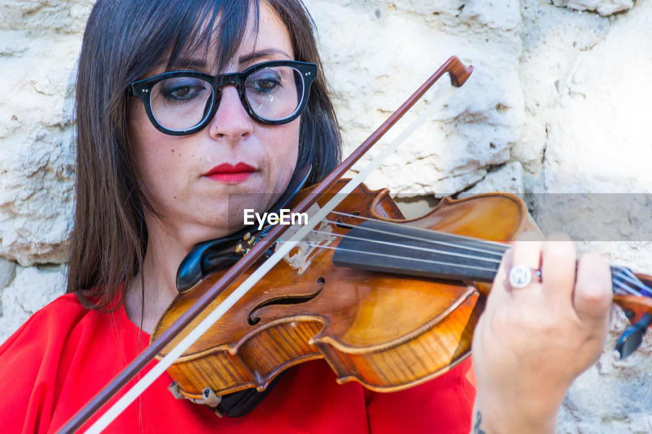 Close-up of woman playing violin against stone wall