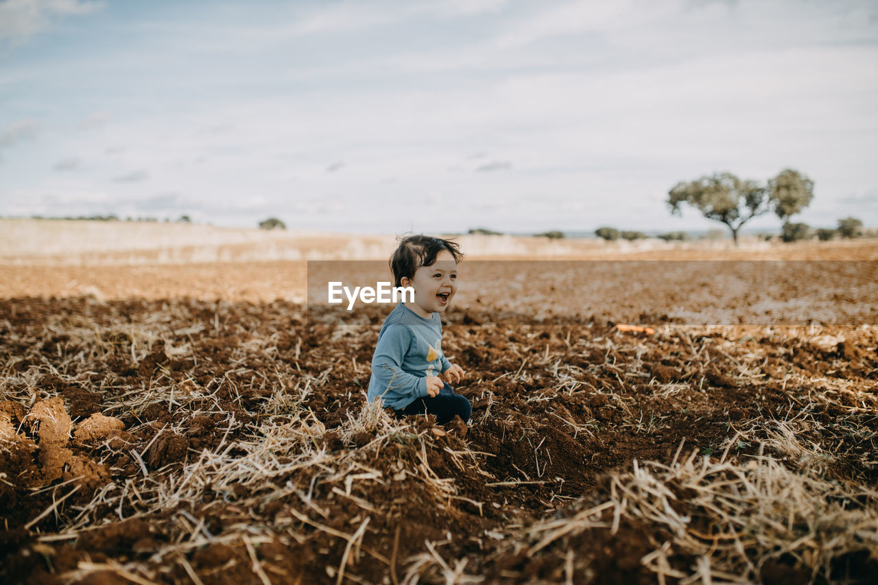 Child sittind on plowed field smiling