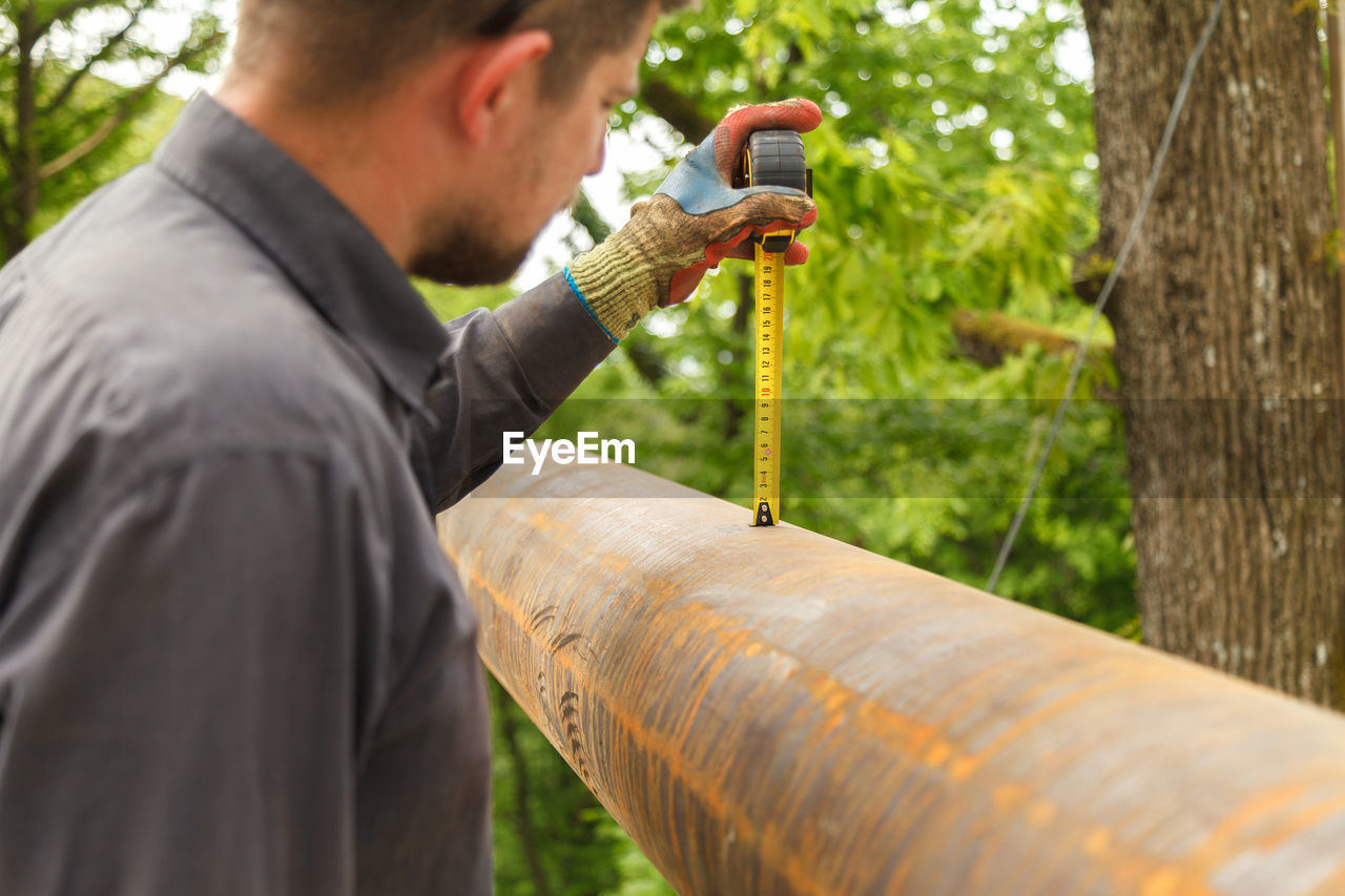 Side view of worker measuring metal against trees