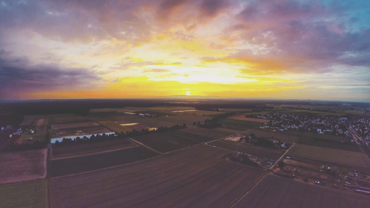 Silhouette of patchwork field and town against sky during sunset