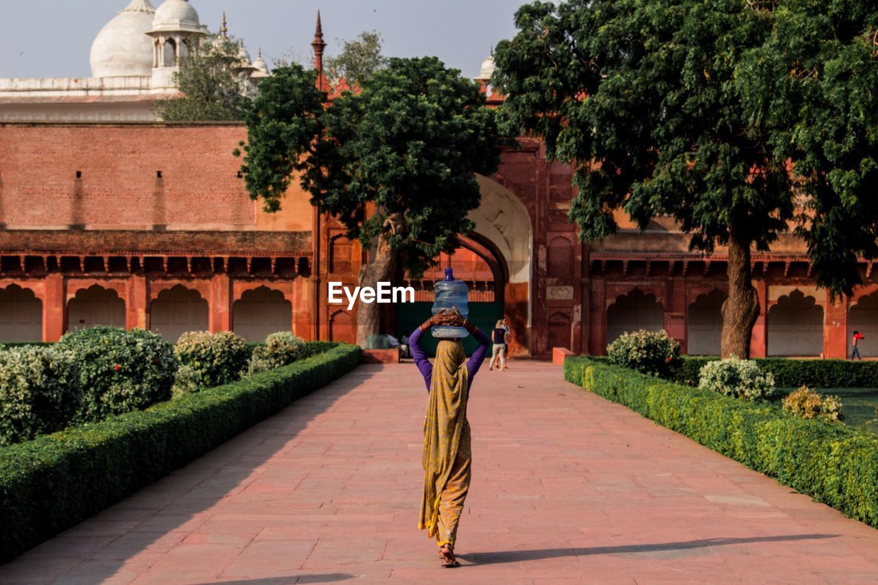 Full length rear view of woman carrying water container against historic building