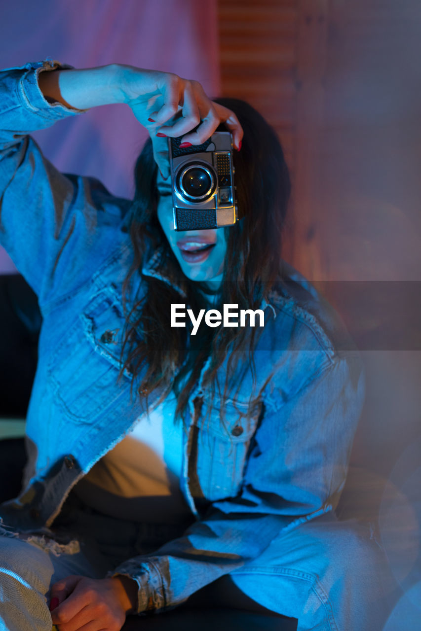 Portrait of woman holding camera against wall