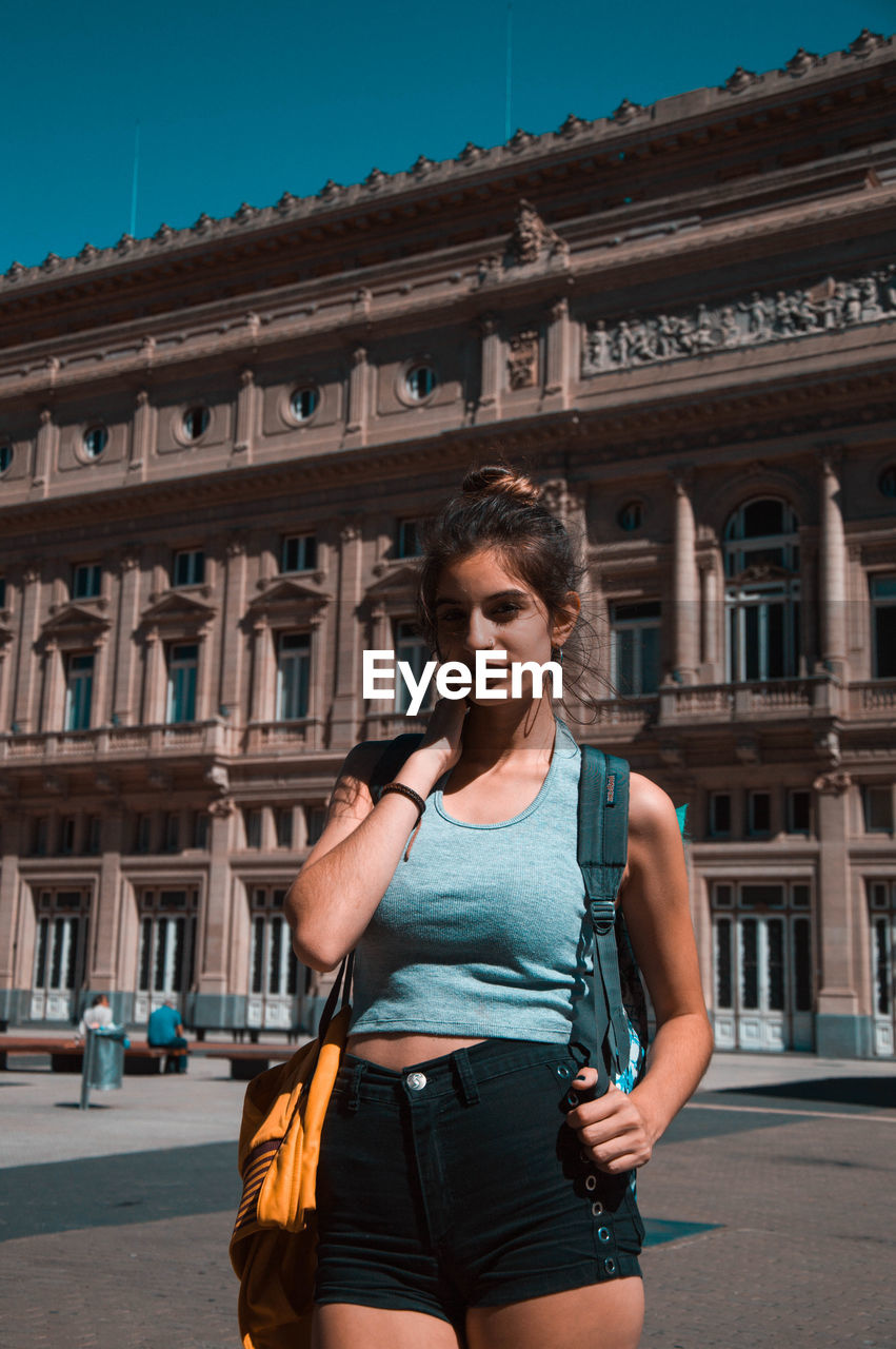 YOUNG WOMAN STANDING BY BUILDING IN CITY