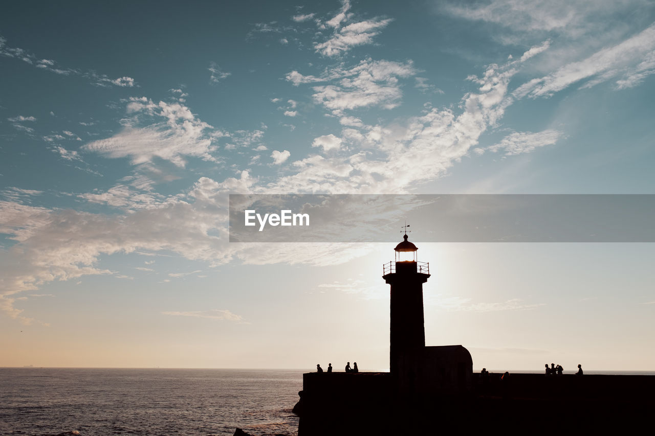 Silhouette lighthouse by sea against sky