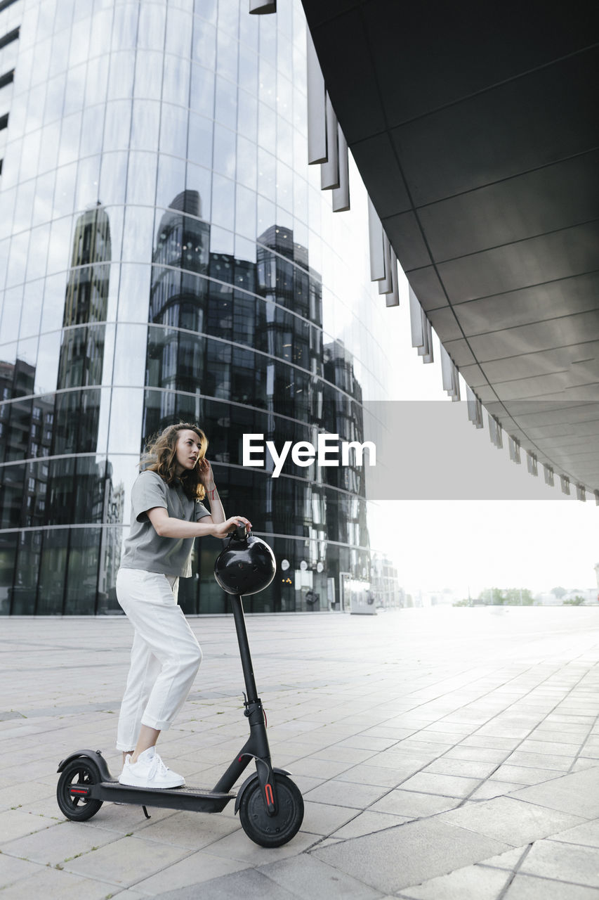Woman with e-scooter and helmet, modern office buildings in the background