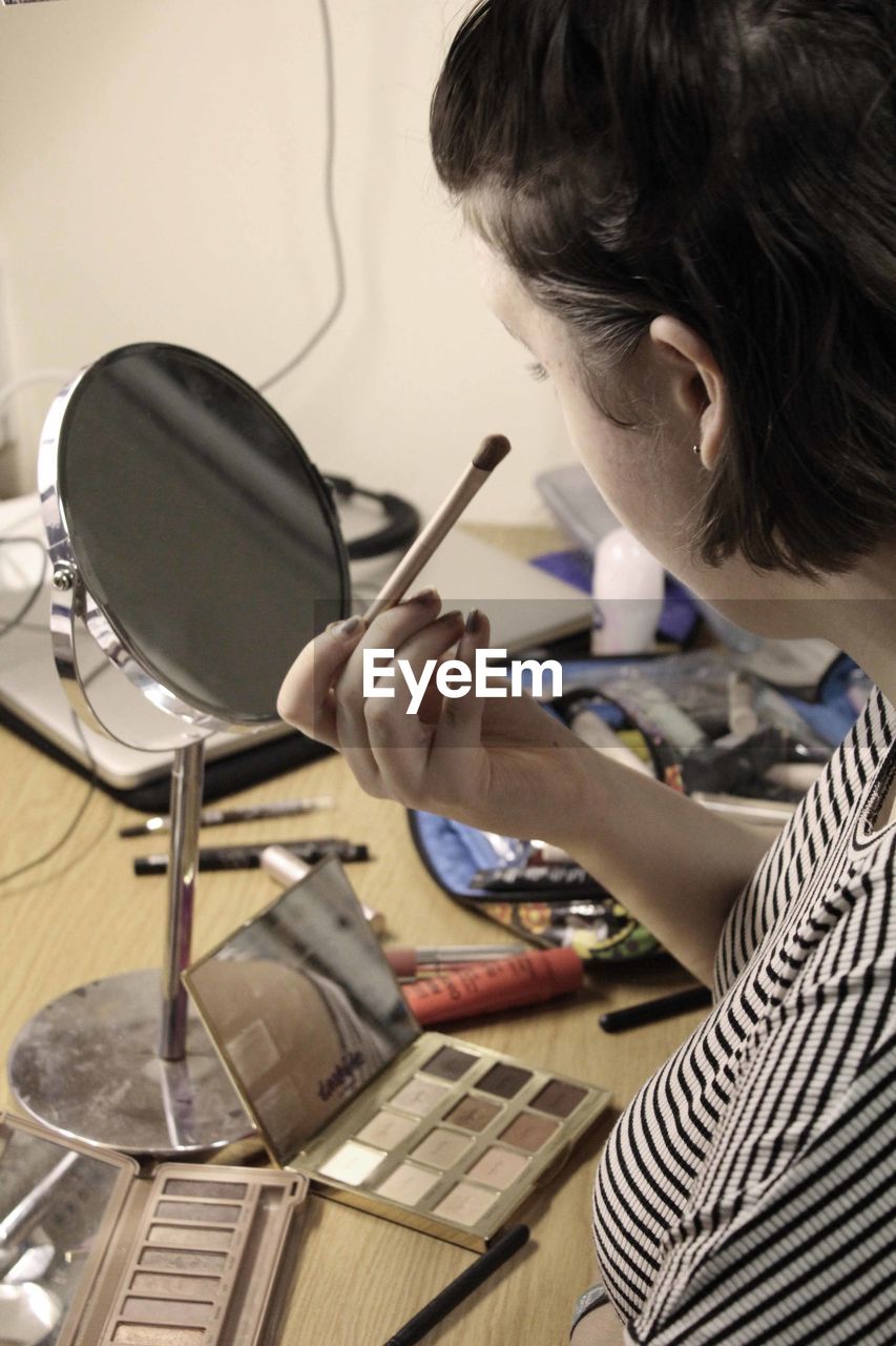 Side view of woman applying make-up on table