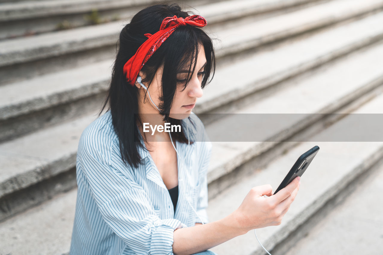 Young woman using phone while sitting on staircase