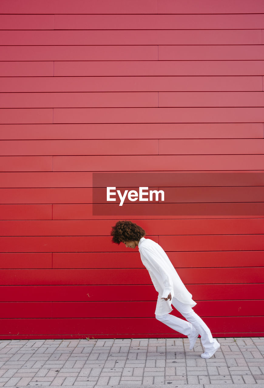 Young woman leaning forward on footpath by red wall