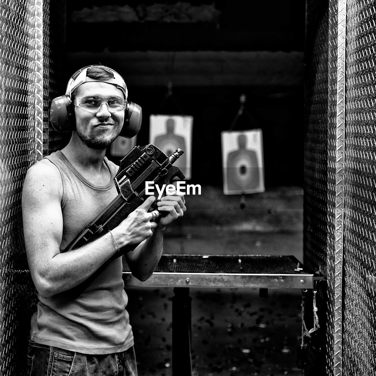 Portrait of young man holding gun while standing at target shooting range