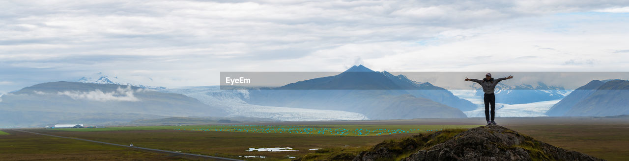 Man standing on rock against mountain range and sky