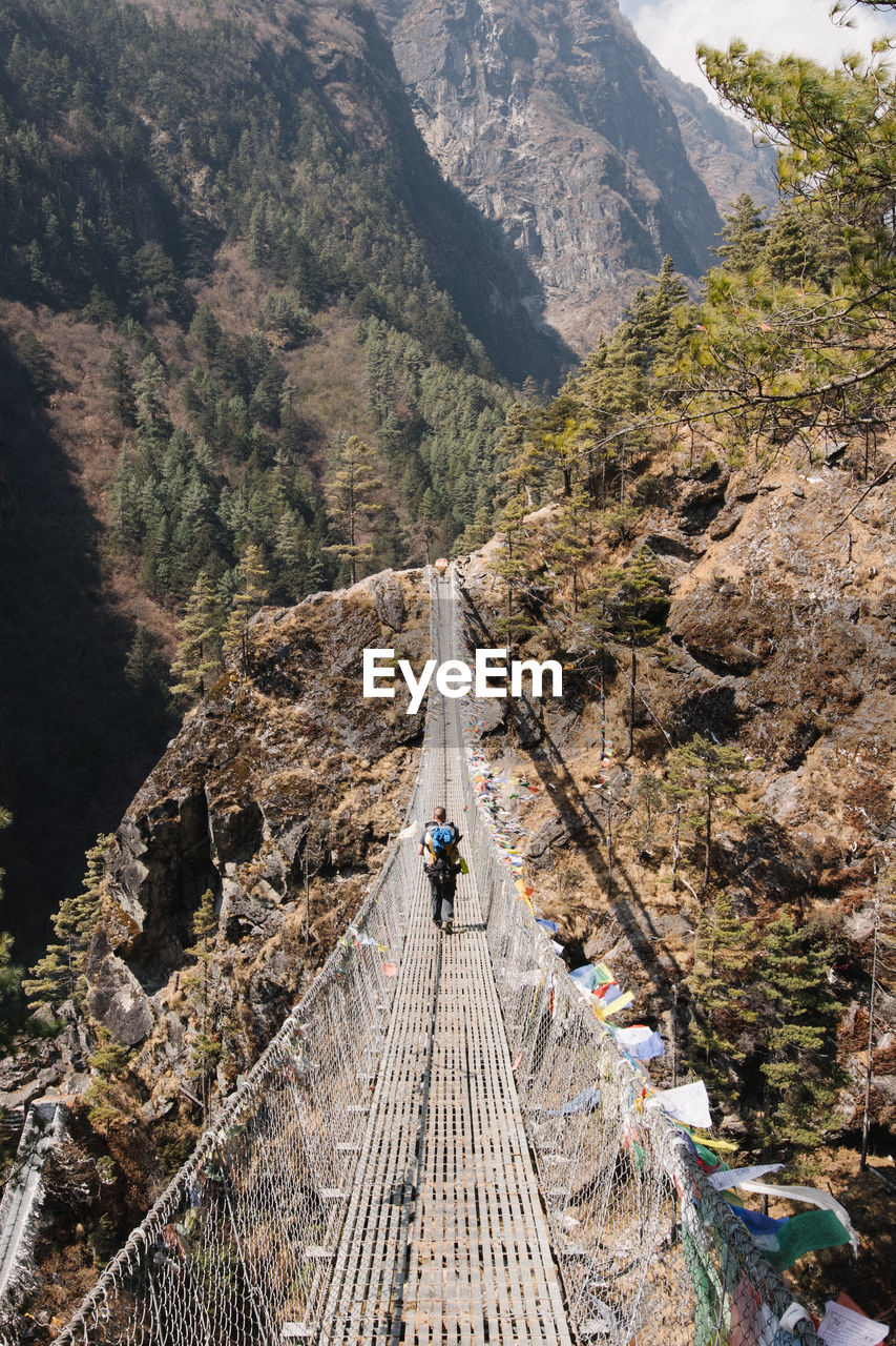 Rear view of man walking on footbridge against mountain