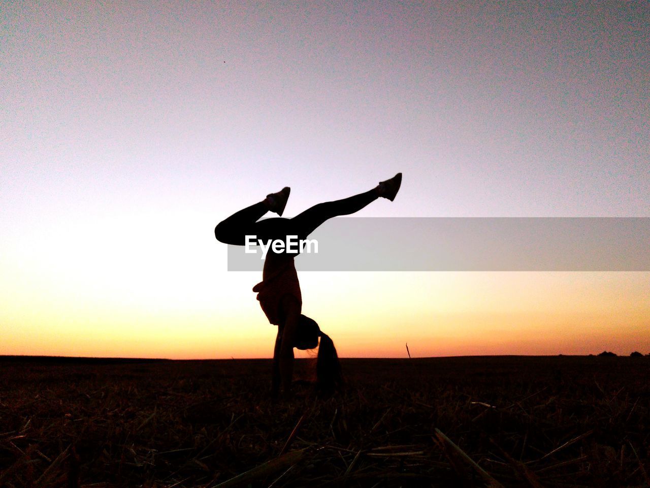 Silhouette woman doing handstand against clear sky during sunset