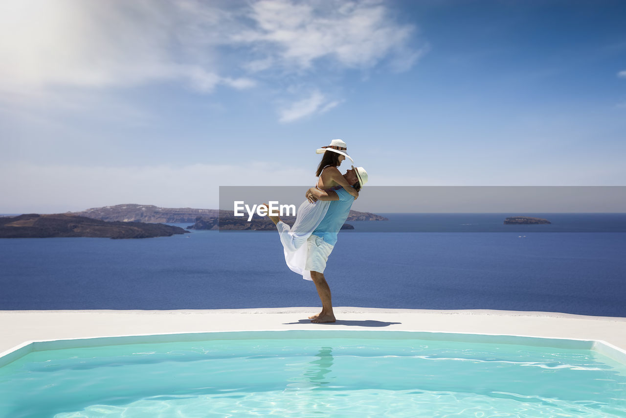 Side view of couple embracing against sea