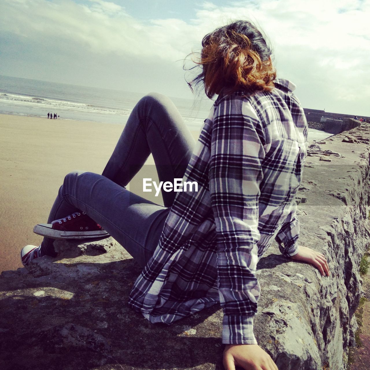 Woman sitting on retaining wall at beach against sky