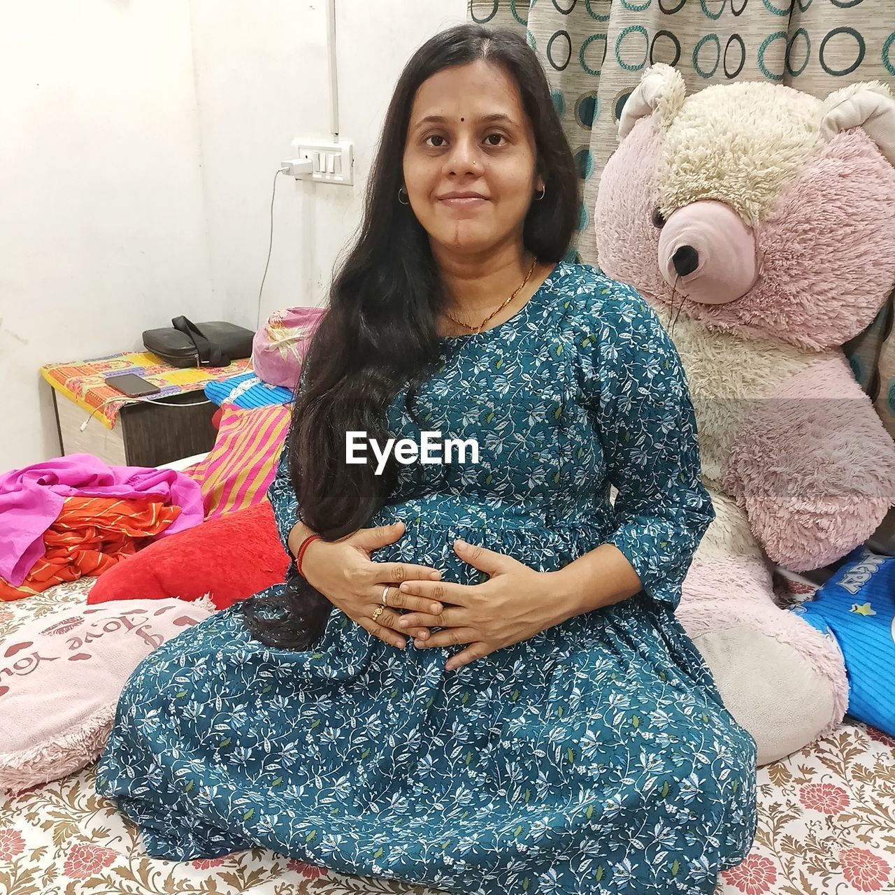 one person, women, adult, looking at camera, sitting, indoors, portrait, smiling, textile, front view, lifestyles, clothing, female, furniture, toy, hairstyle, home interior, three quarter length, happiness, art, long hair, domestic room, emotion, pattern, black hair, brown hair, young adult, dress, casual clothing, domestic life