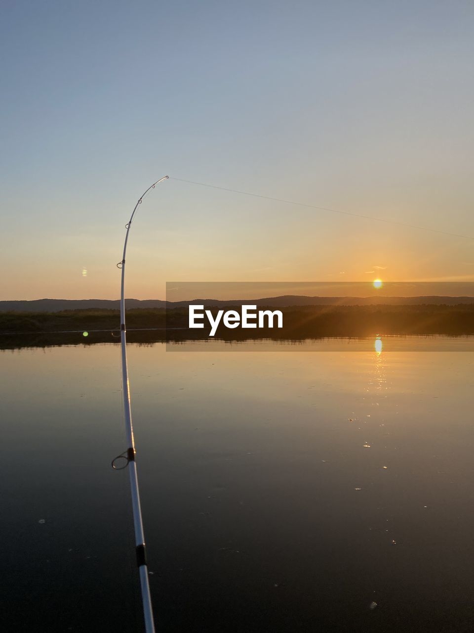Scenic view off fishingrod on lake against sky during sunset