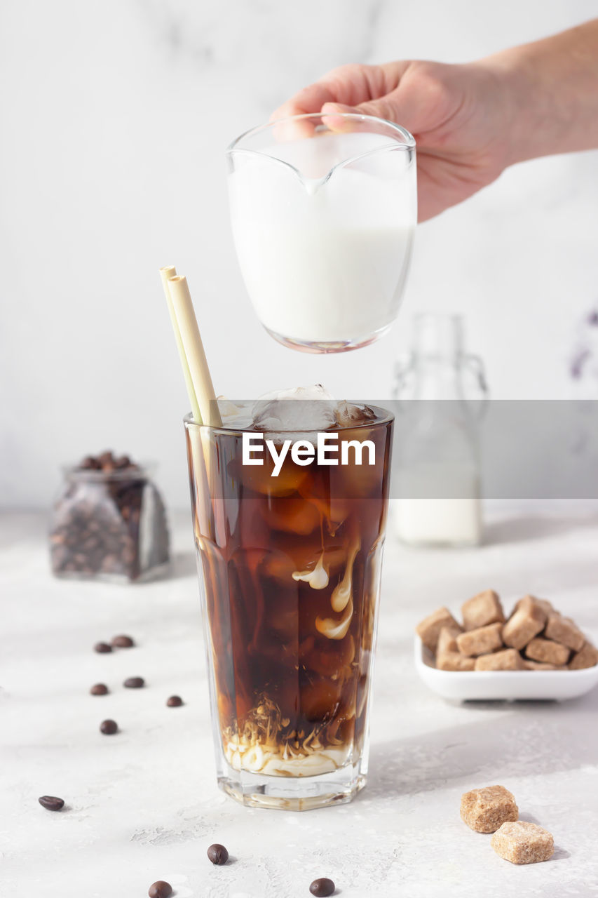 Iced coffee in a tall glass with cream being poured into it showing the texture of the drink. 