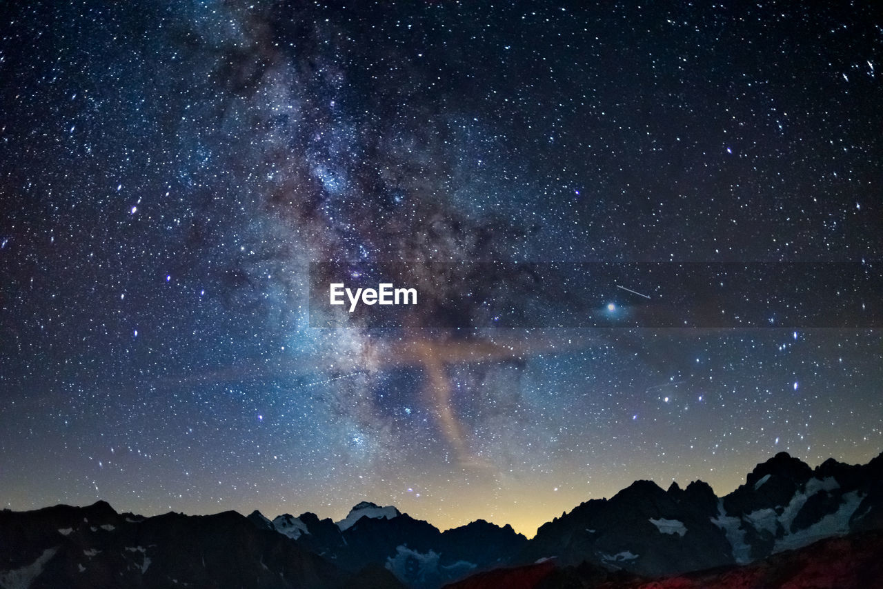 LOW ANGLE VIEW OF MOUNTAINS AGAINST STAR FIELD