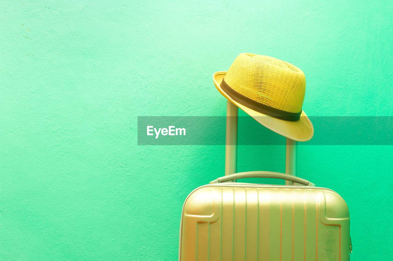 Close-up of hat and suitcase against colored background
