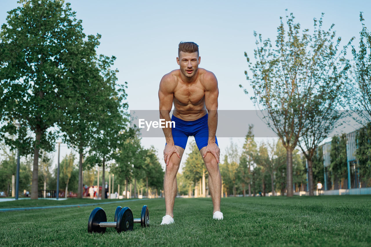 full length of shirtless man exercising on field