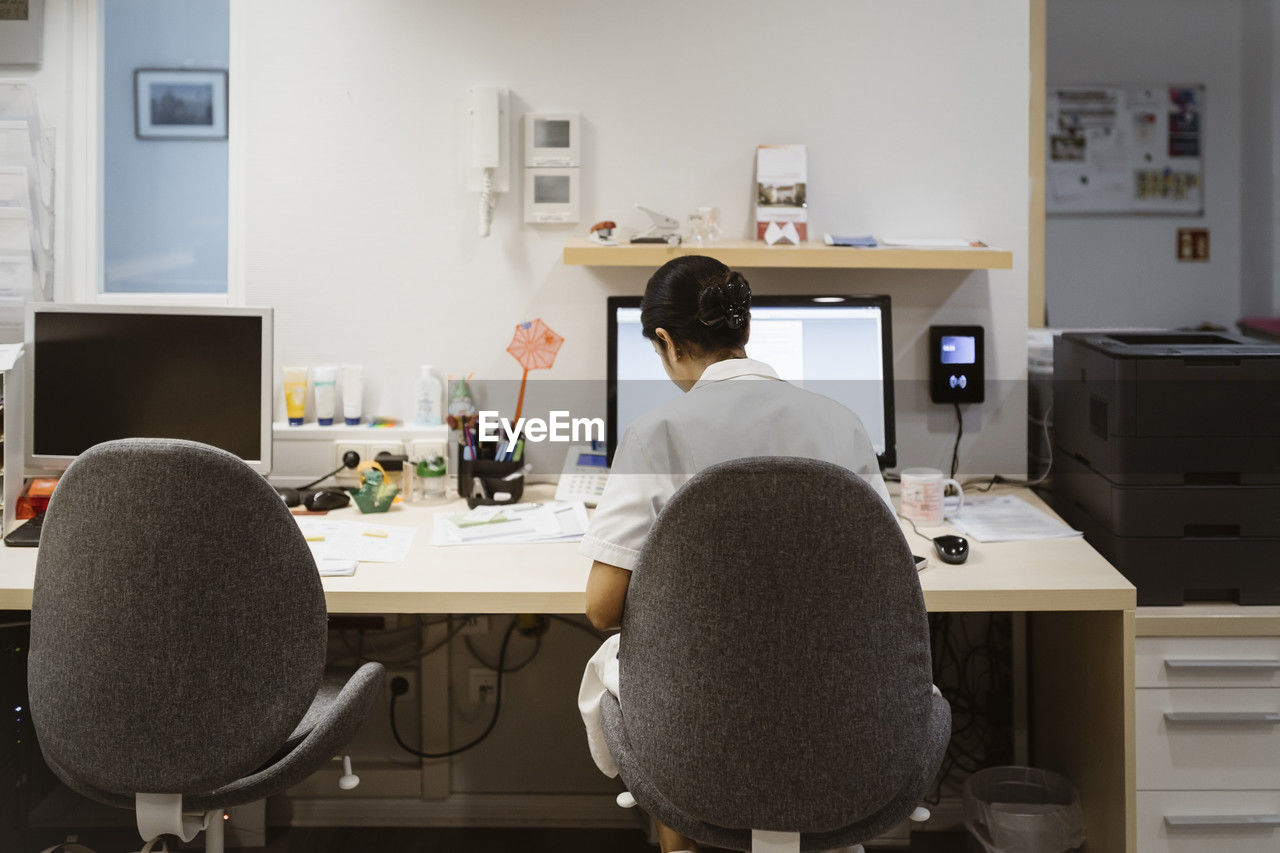 Rear view of female healthcare worker sitting on chair and working in clinic