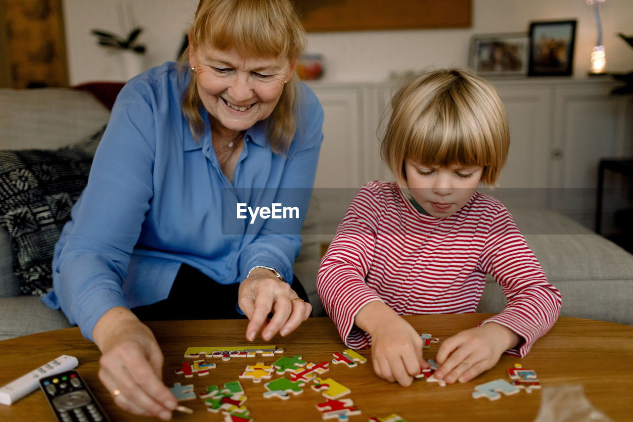 Boy playing jigsaw puzzle with smiling grandmother at home