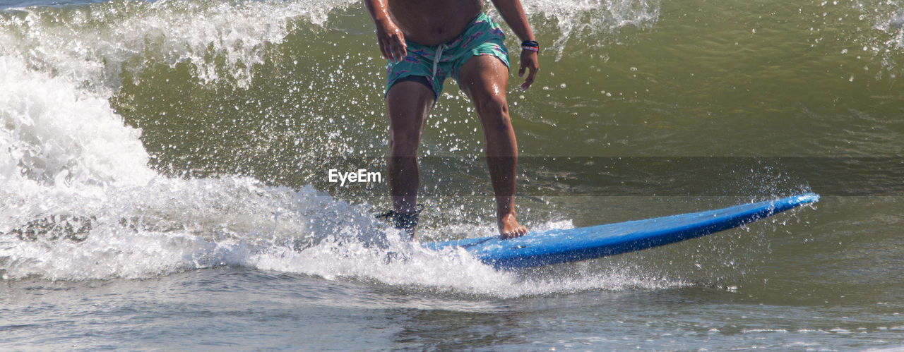 Side view of a man riding his blue surfboard surfing at gilgo beach on long island.