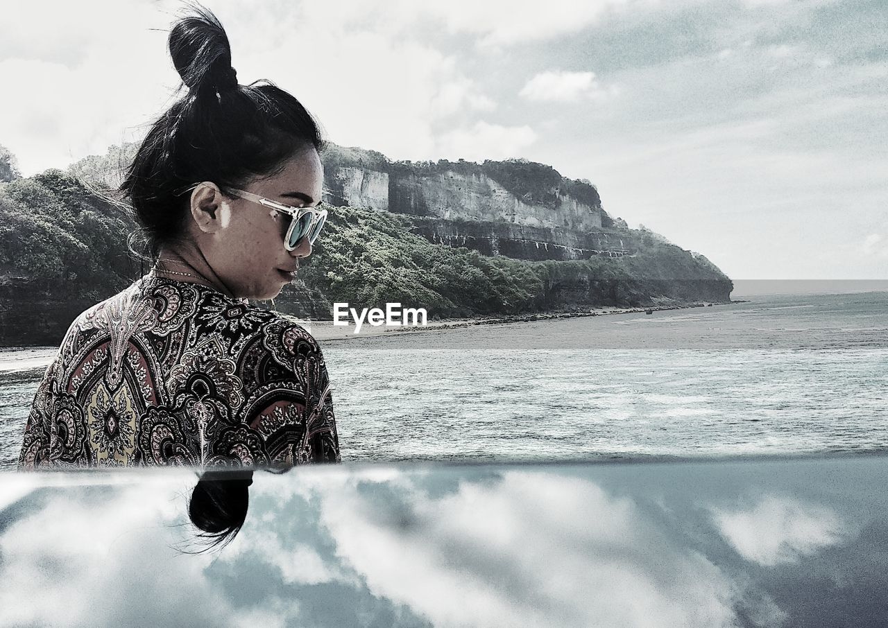 MAN LOOKING AT SEA BY SUNGLASSES AGAINST SKY