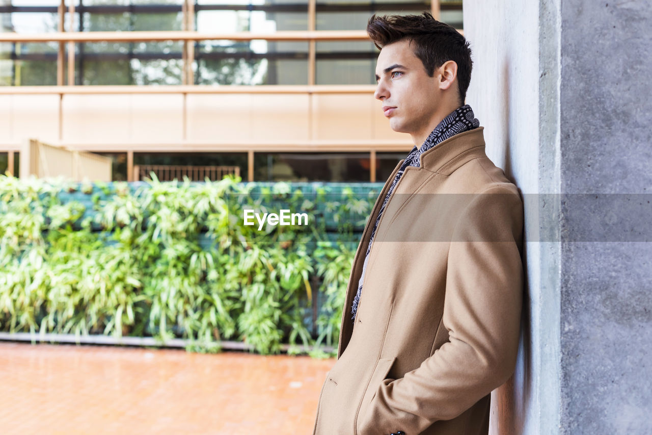 Thoughtful young man standing by wall