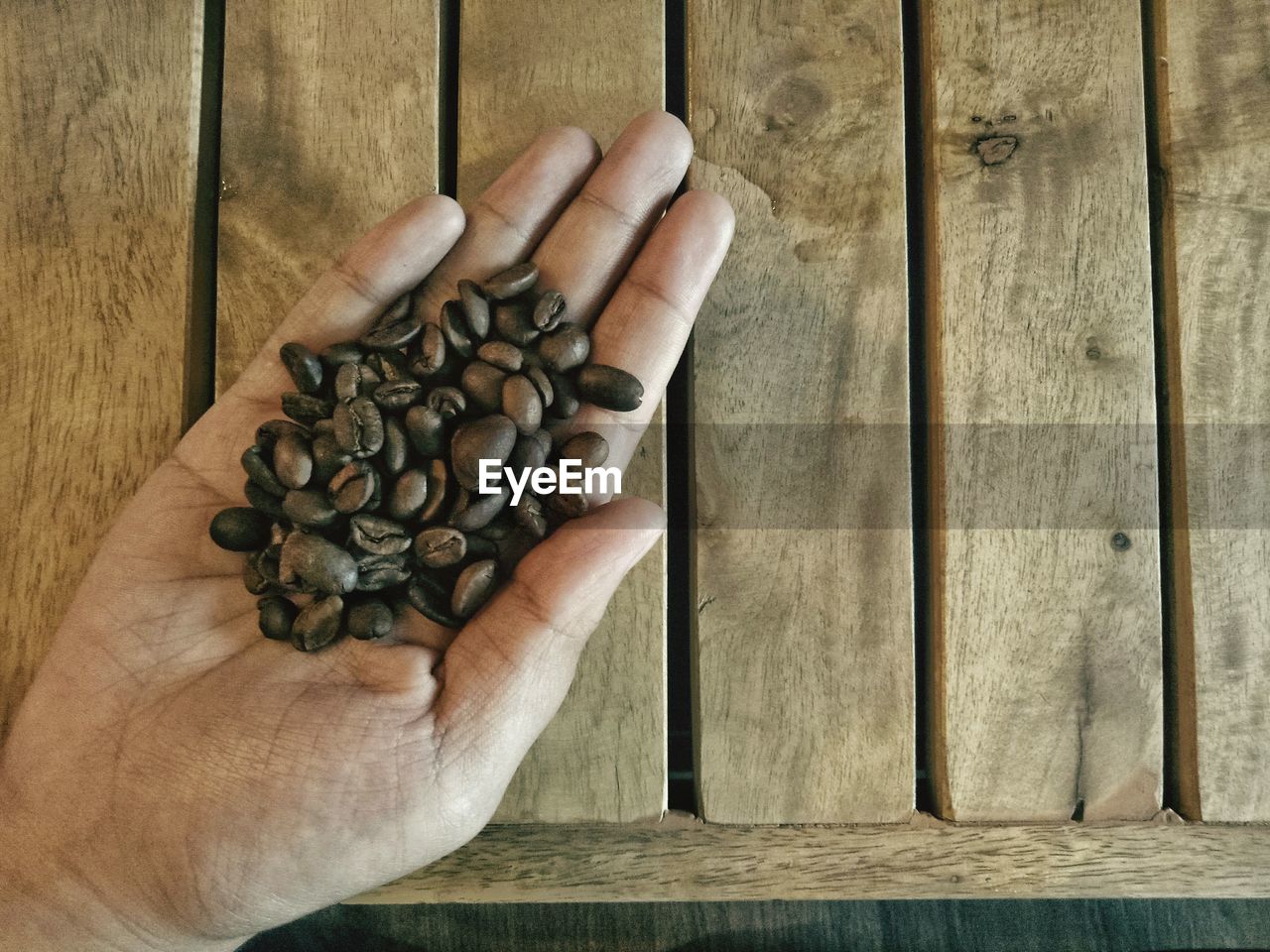 Close-up of human hand holding roasted coffee beans over table