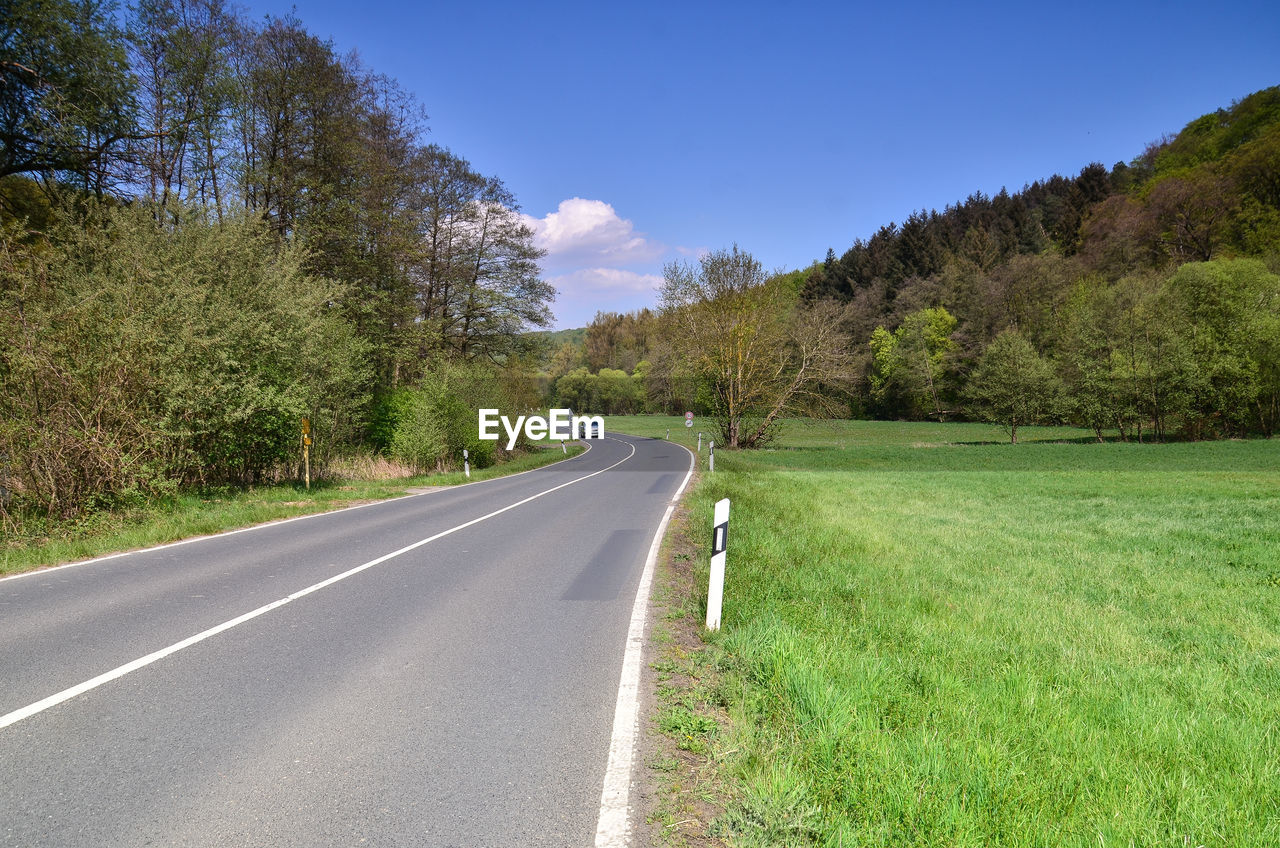 ROAD AMIDST TREES AND GRASS AGAINST SKY