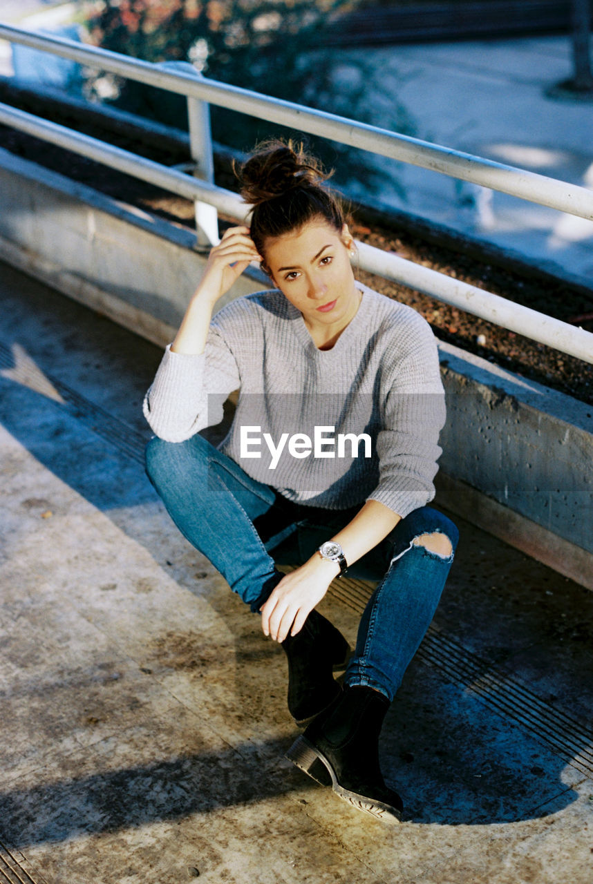 Full length portrait of young woman sitting by railing