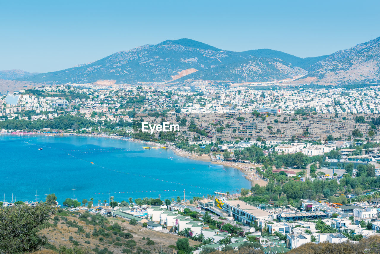 High angle view of city by sea against blue sky