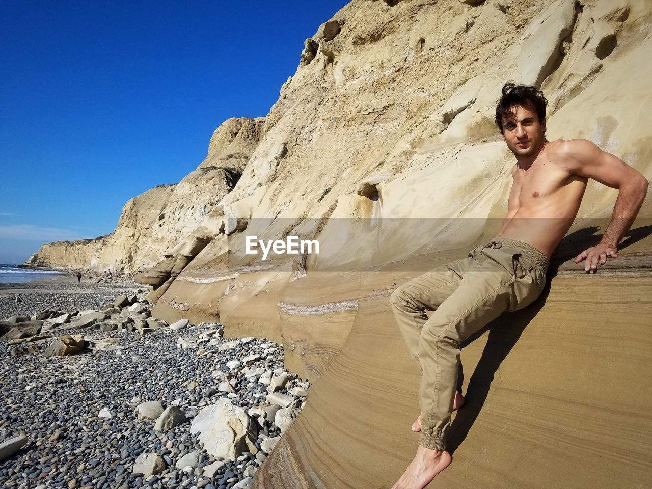 FULL LENGTH OF SHIRTLESS MAN STANDING ON ROCK AGAINST SKY