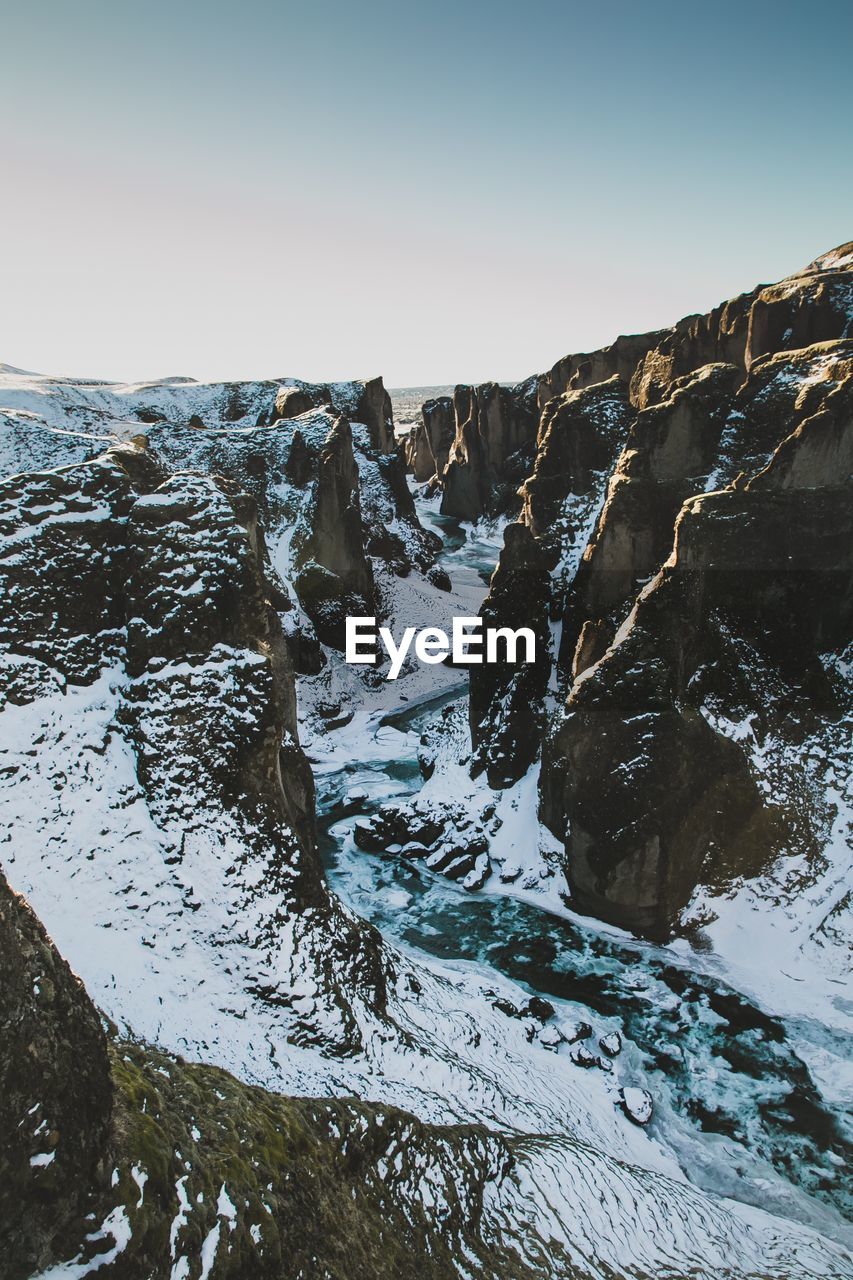 Scenic view of river flowing amidst snow covered mountains against sky