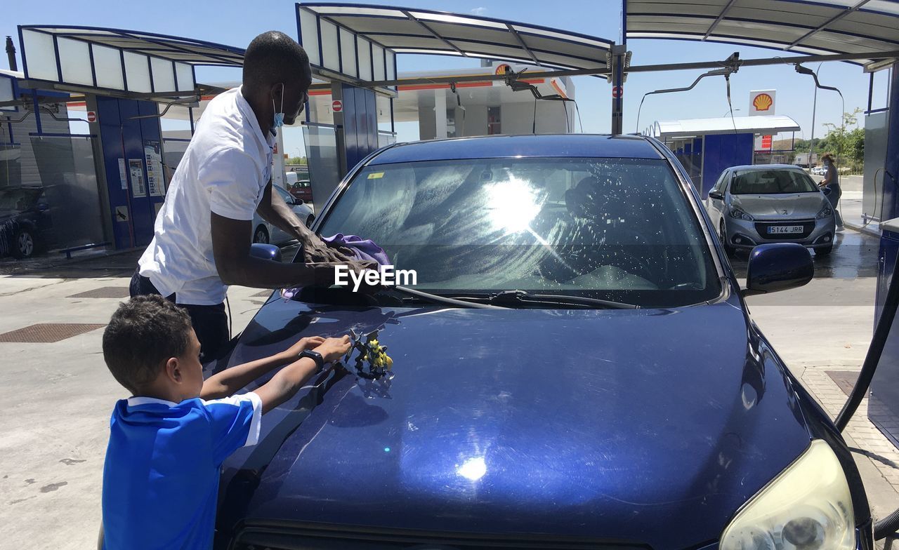 Father son adult child gas station car wash working  cleaning  polishing their dark blue car