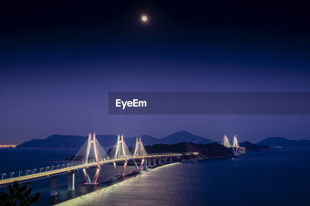 Illuminated bridge over sea against clear sky at night