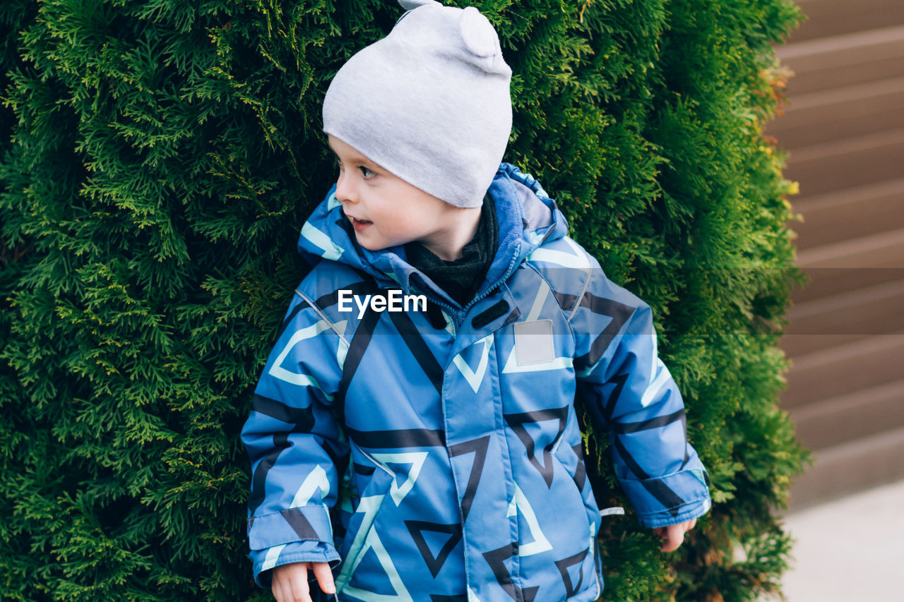 Child peeking out from behind a tree outdoors. playful and cheerful boy person