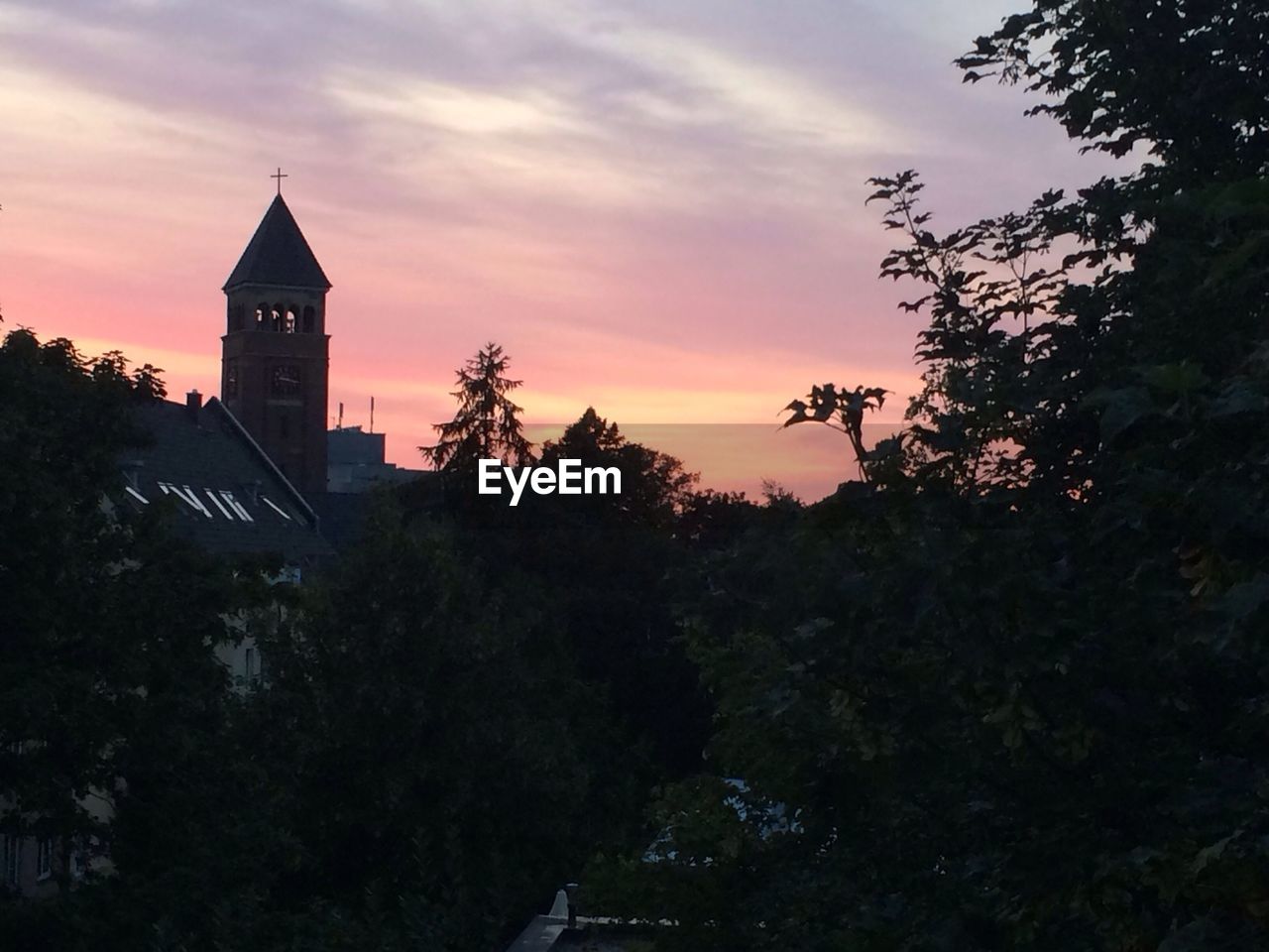 Church by trees against orange sky