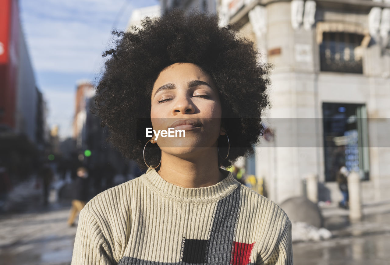 Afro woman with eyes closed standing in city